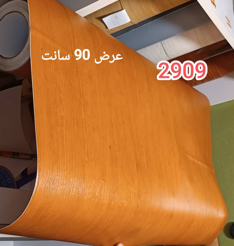 رول نیمه‌باز برچسب کابینت طرح چوب طبیعی قهوه‌ای نارنجی کد ۲۹۰۹ عرض ۹۰ سانت روی سطح سفید کارگاهی